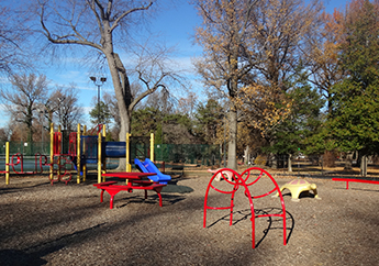 Red and blue outdoor playground surrounded by leafless trees during the winter